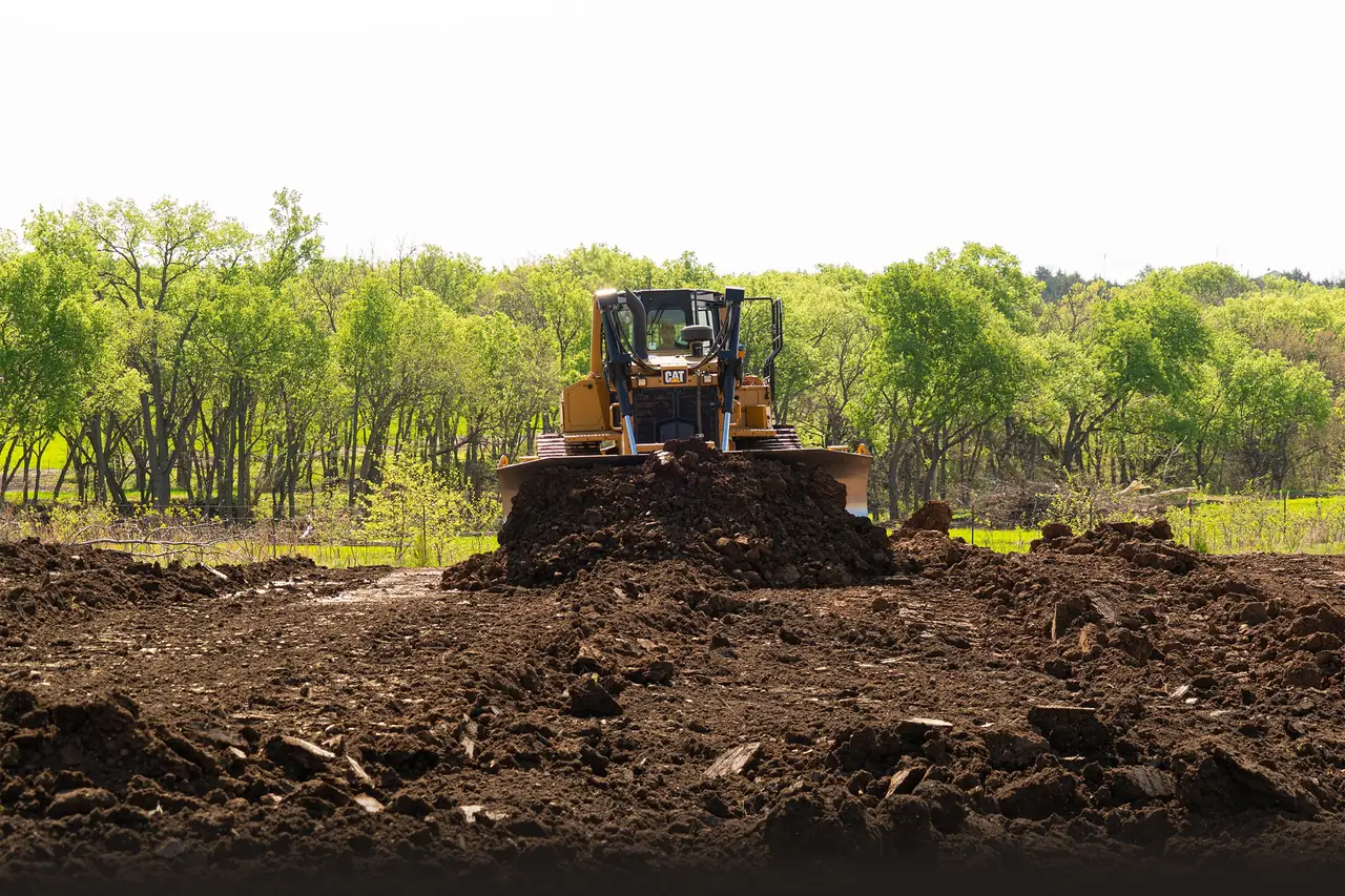 Yellow crawler dozer pushing a pile of dirt across cleared ground