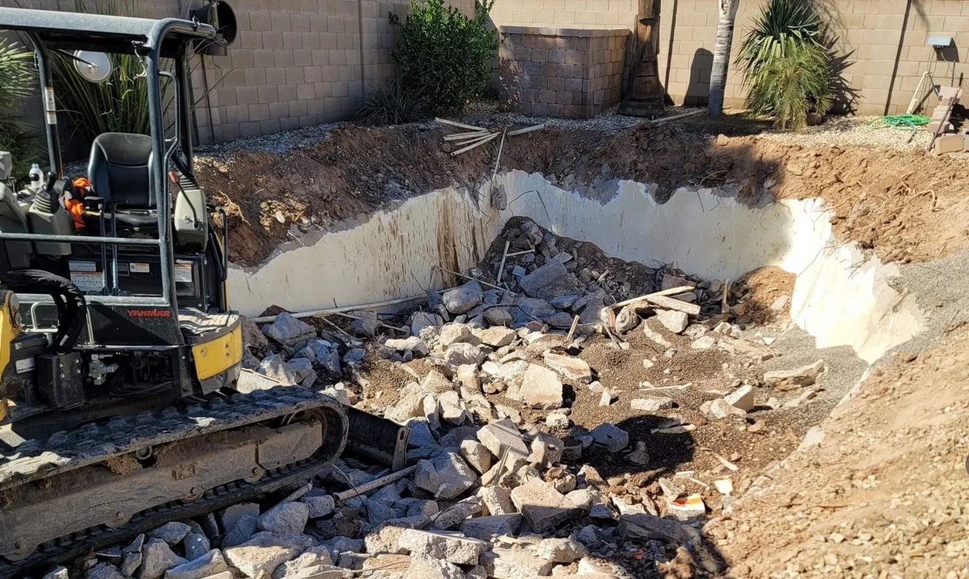 Mini excavator beside a broken out pool shell with rubble ready to load